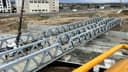 Köprünün yandan görünümü; iki kafes kiriş paralel duruyor, altta betonarme kanal, solda vinç ve servis aracı