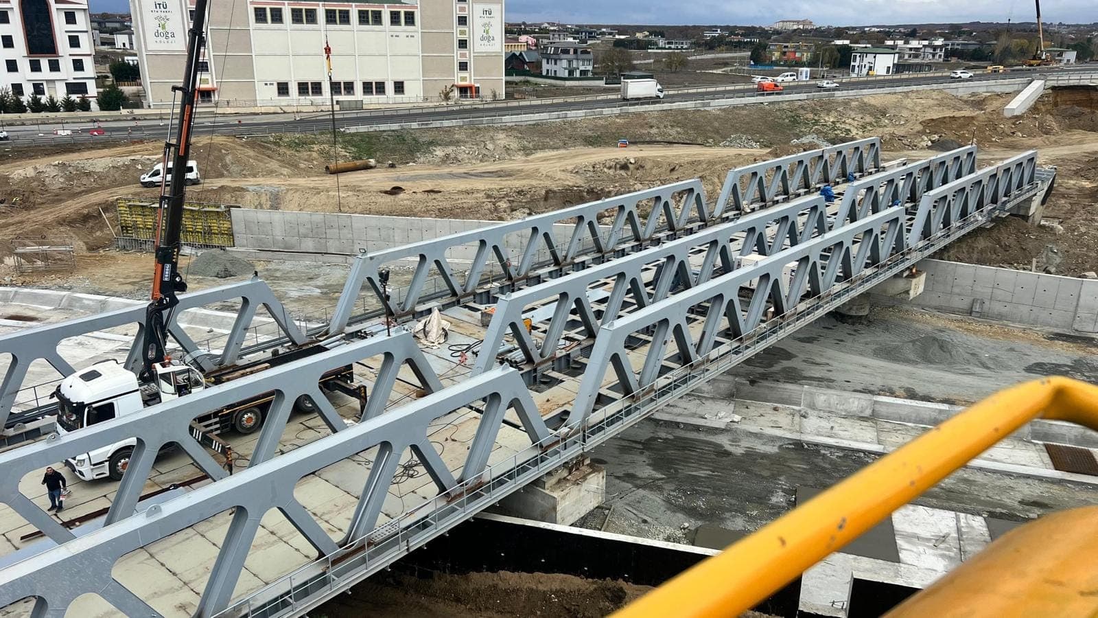 Köprünün yandan görünümü; iki kafes kiriş paralel duruyor, altta betonarme kanal, solda vinç ve servis aracı