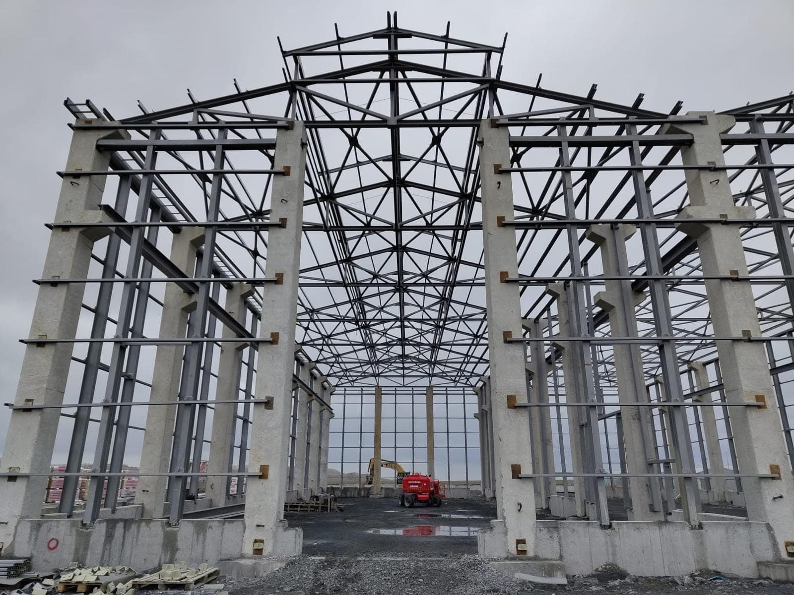 Hangarın içinden boydan boya görünüm; iki yanda beton kolon sıraları, üstte kafes makaslar ve aşıklar, uçta açık cephe